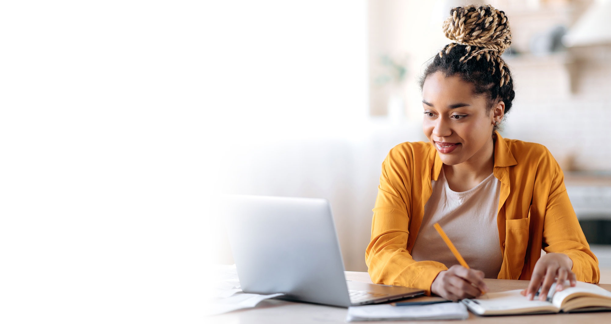 Woman writing in a journal while working on a laptop